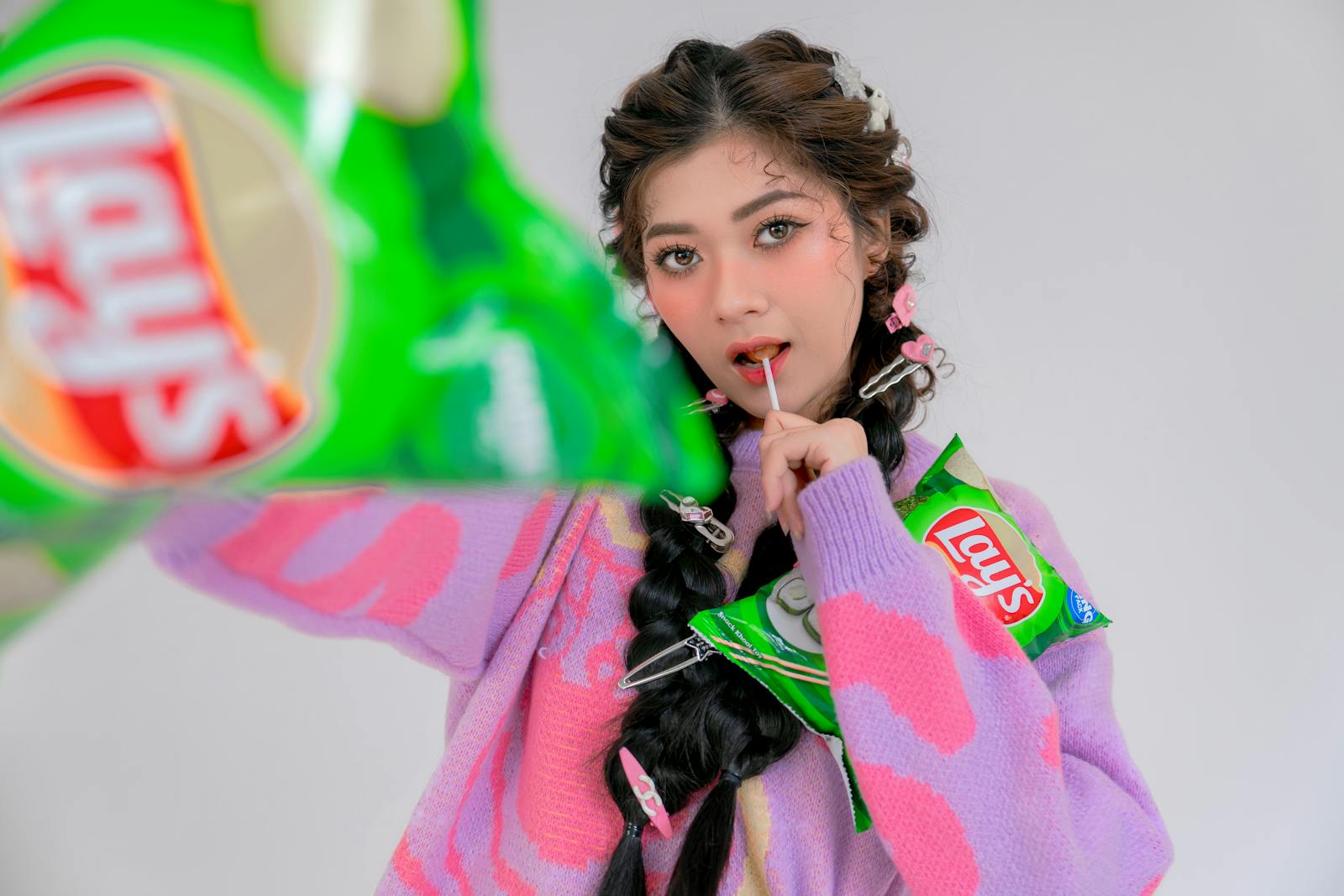 Trendy woman in colorful attire holding Lay's chips bag with playful expression.