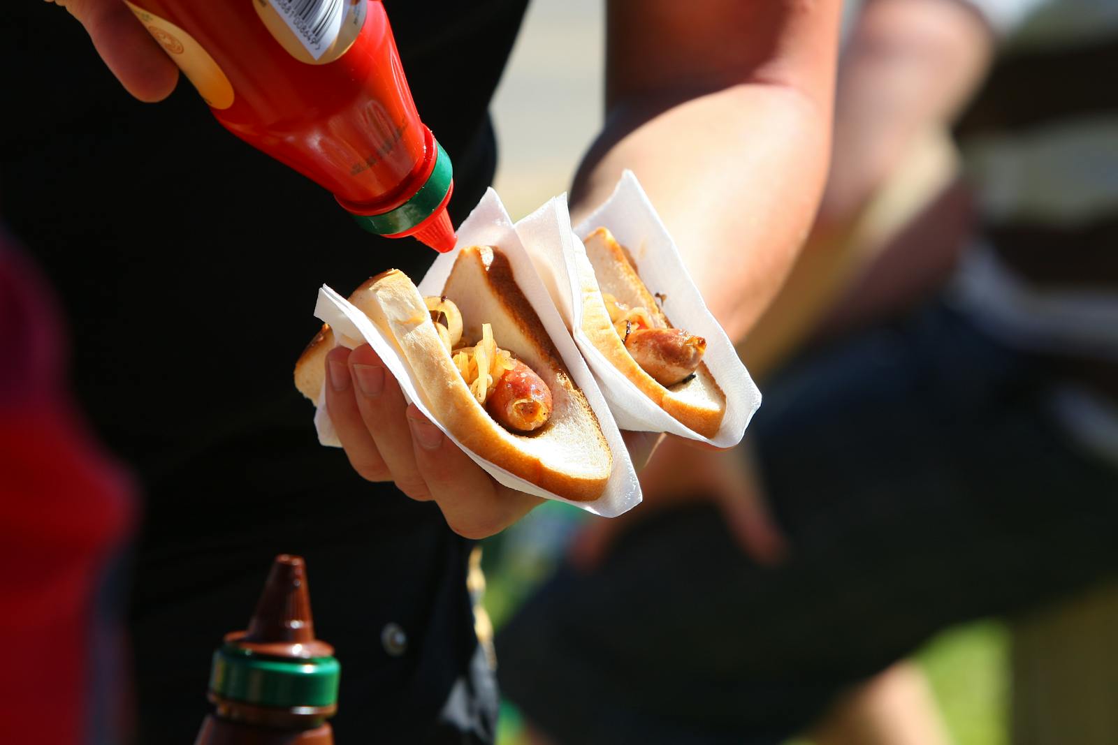 Close-up of a person adding ketchup to hot dogs, highlighting a casual outdoor meal.