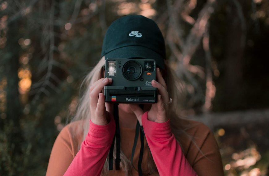 A woman captures a moment using a Polaroid camera in a picturesque autumn forest setting.