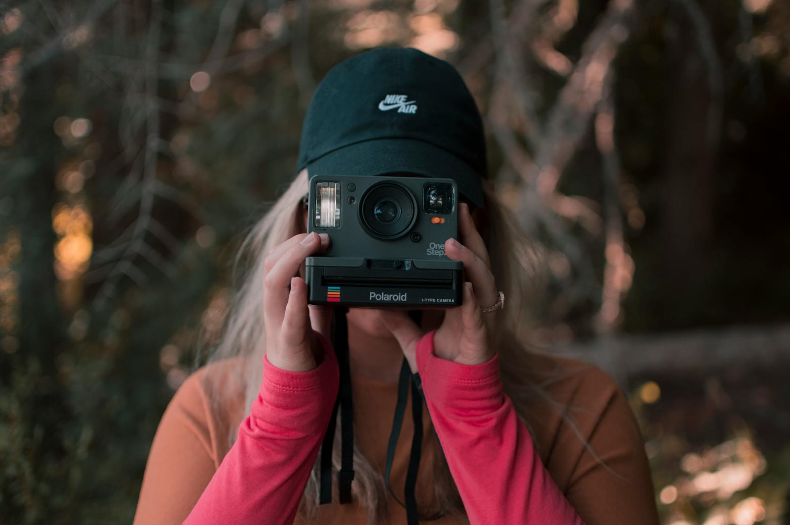 A woman captures a moment using a Polaroid camera in a picturesque autumn forest setting.