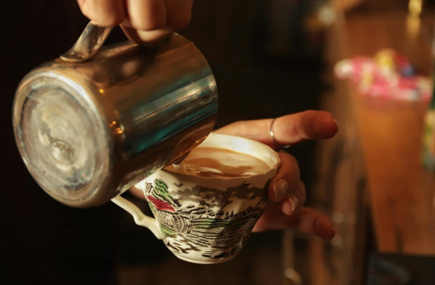Close-up of a barista pouring coffee into a vintage teacup at a cafe.