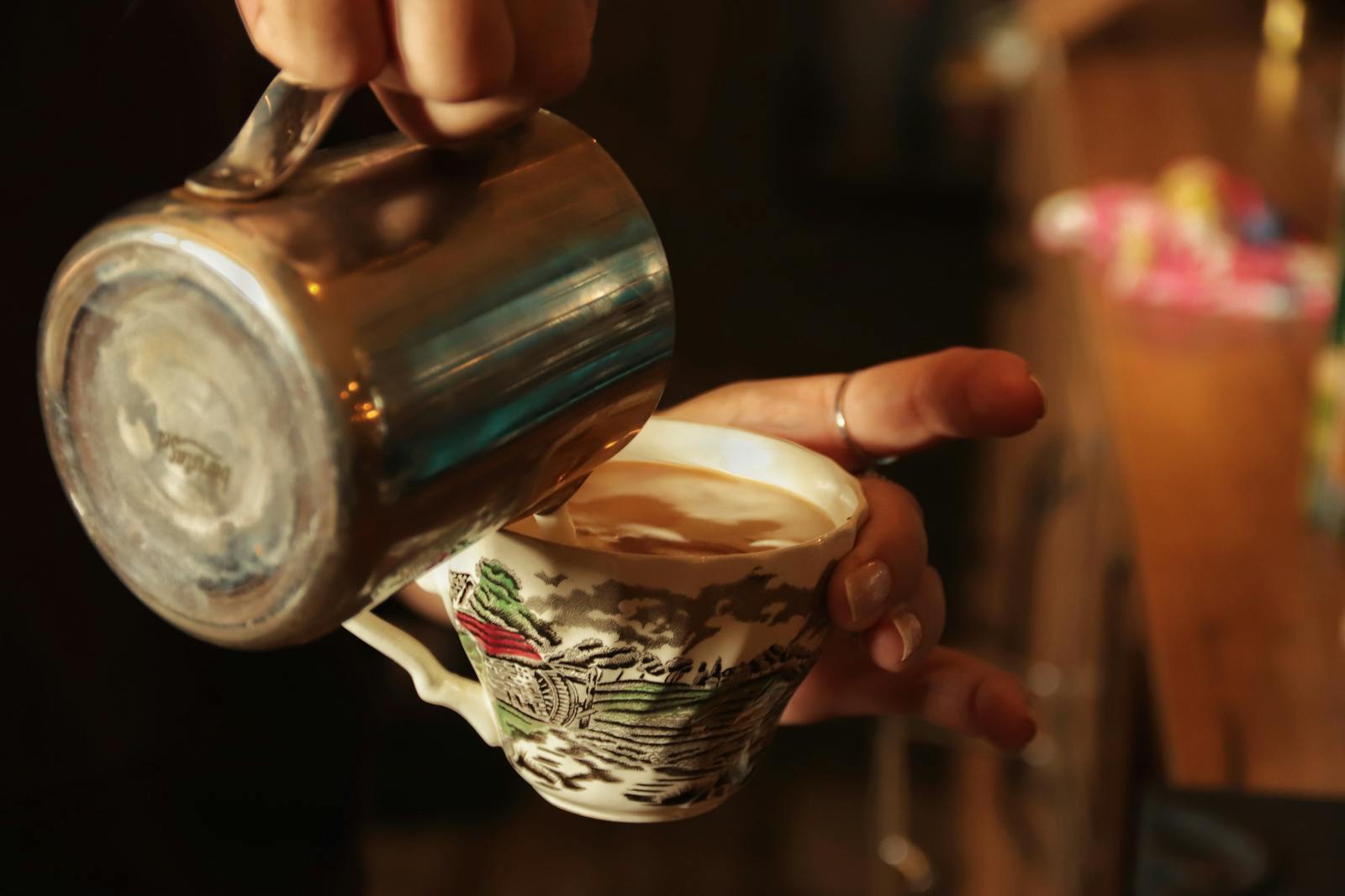 Close-up of a barista pouring coffee into a vintage teacup at a cafe.