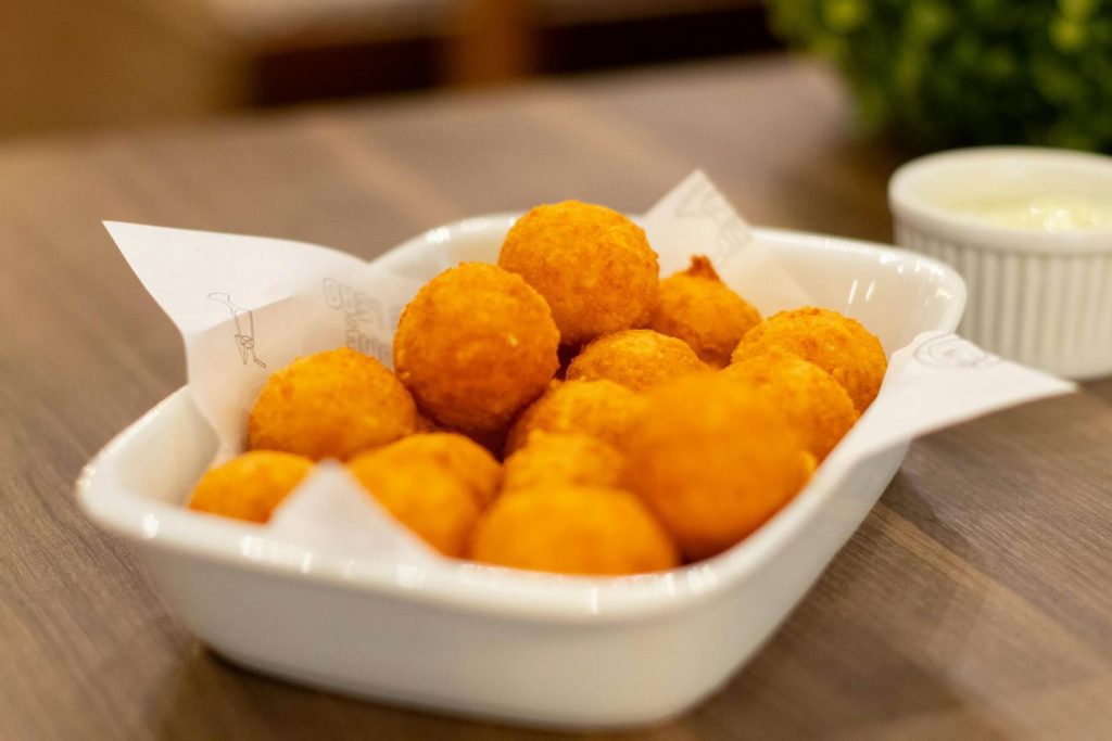 A close-up of crispy cheese balls served in a white dish on a wooden table.