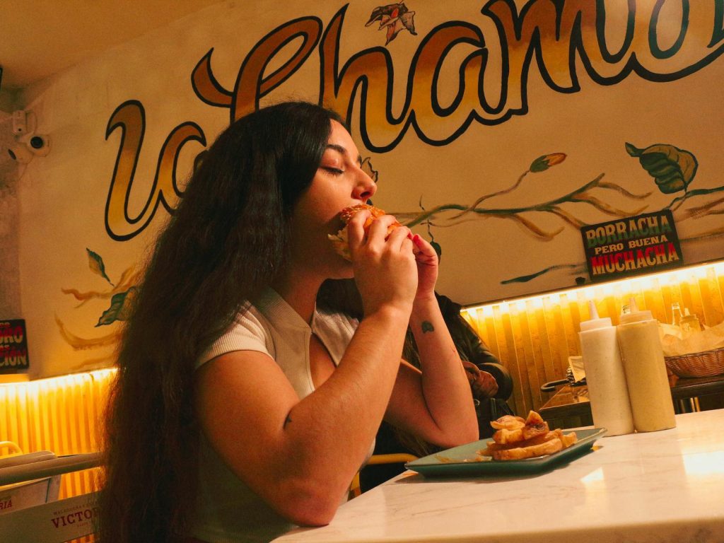 Woman eating a burger at a lively diner with colorful decor.