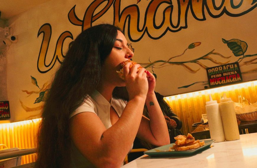 Woman eating a burger at a lively diner with colorful decor.