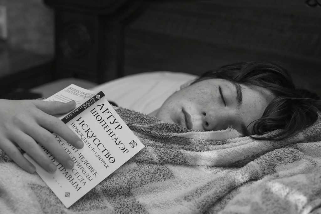 A teenage boy rests with a book in a cozy black and white setting.