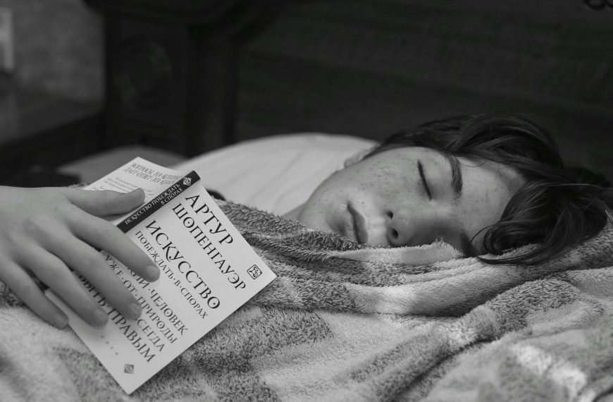 A teenage boy rests with a book in a cozy black and white setting.