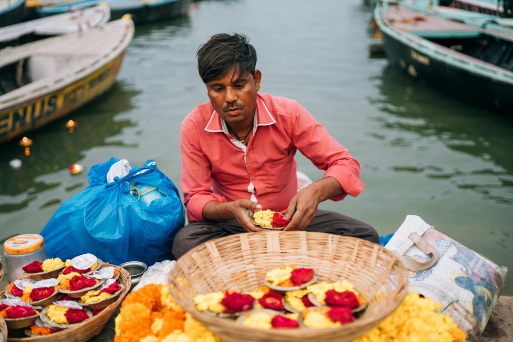 Man arranging flower offerings by the Ganges in Varanasi, capturing cultural essence.