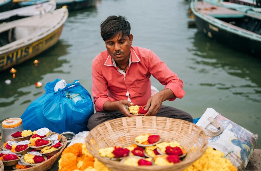 Man arranging flower offerings by the Ganges in Varanasi, capturing cultural essence.