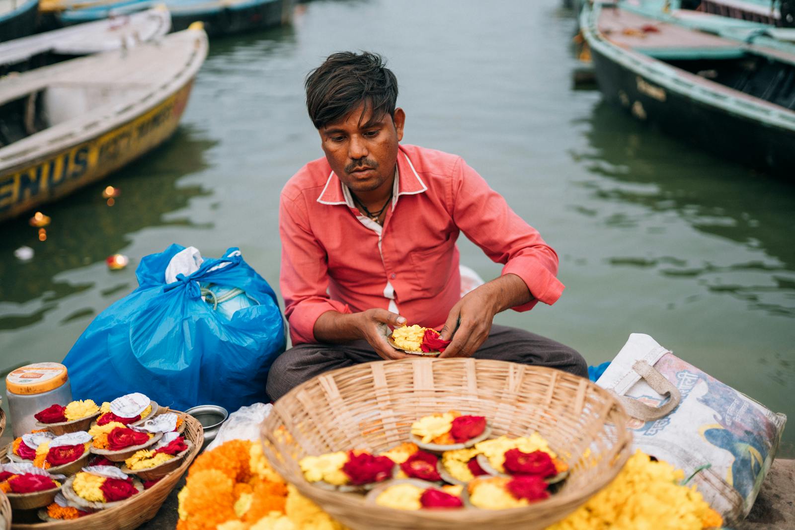 Man arranging flower offerings by the Ganges in Varanasi, capturing cultural essence.