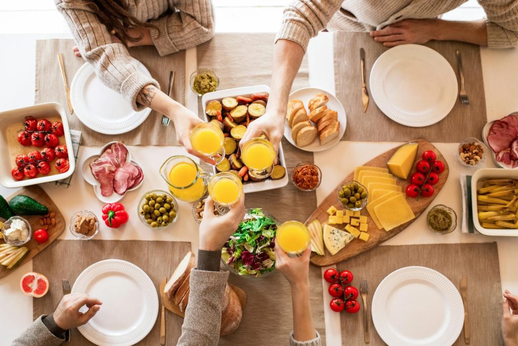 Top view of a family toasting at a lunch table with cheese, olives, and fresh salads.