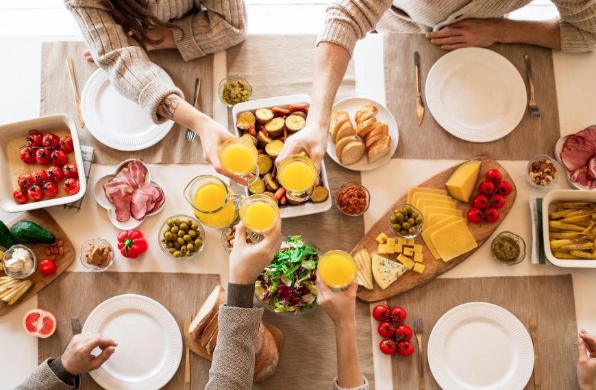 Top view of a family toasting at a lunch table with cheese, olives, and fresh salads.