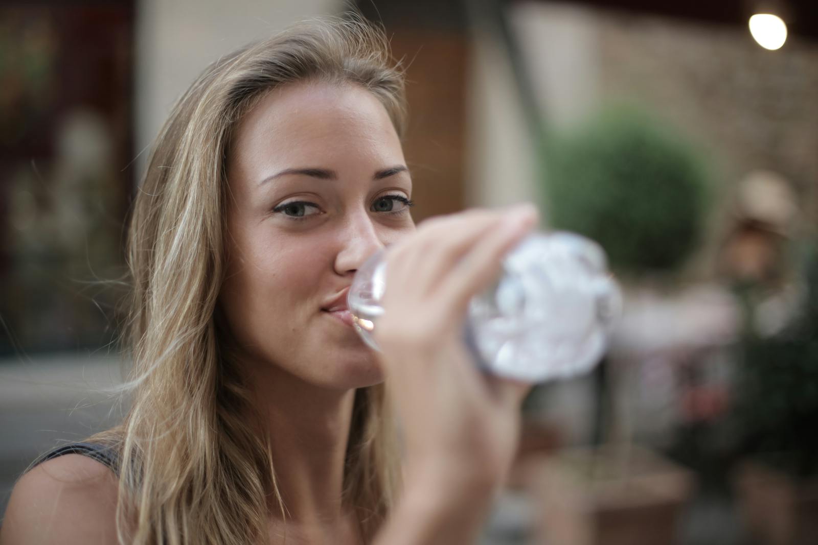 Portrait of a smiling woman drinking bottled water outdoors, enjoying hydration and relaxation.