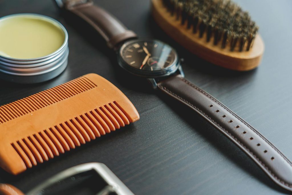 Flat lay image of grooming items with an elegant leather wristwatch on a dark surface.