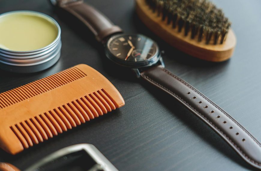 Flat lay image of grooming items with an elegant leather wristwatch on a dark surface.