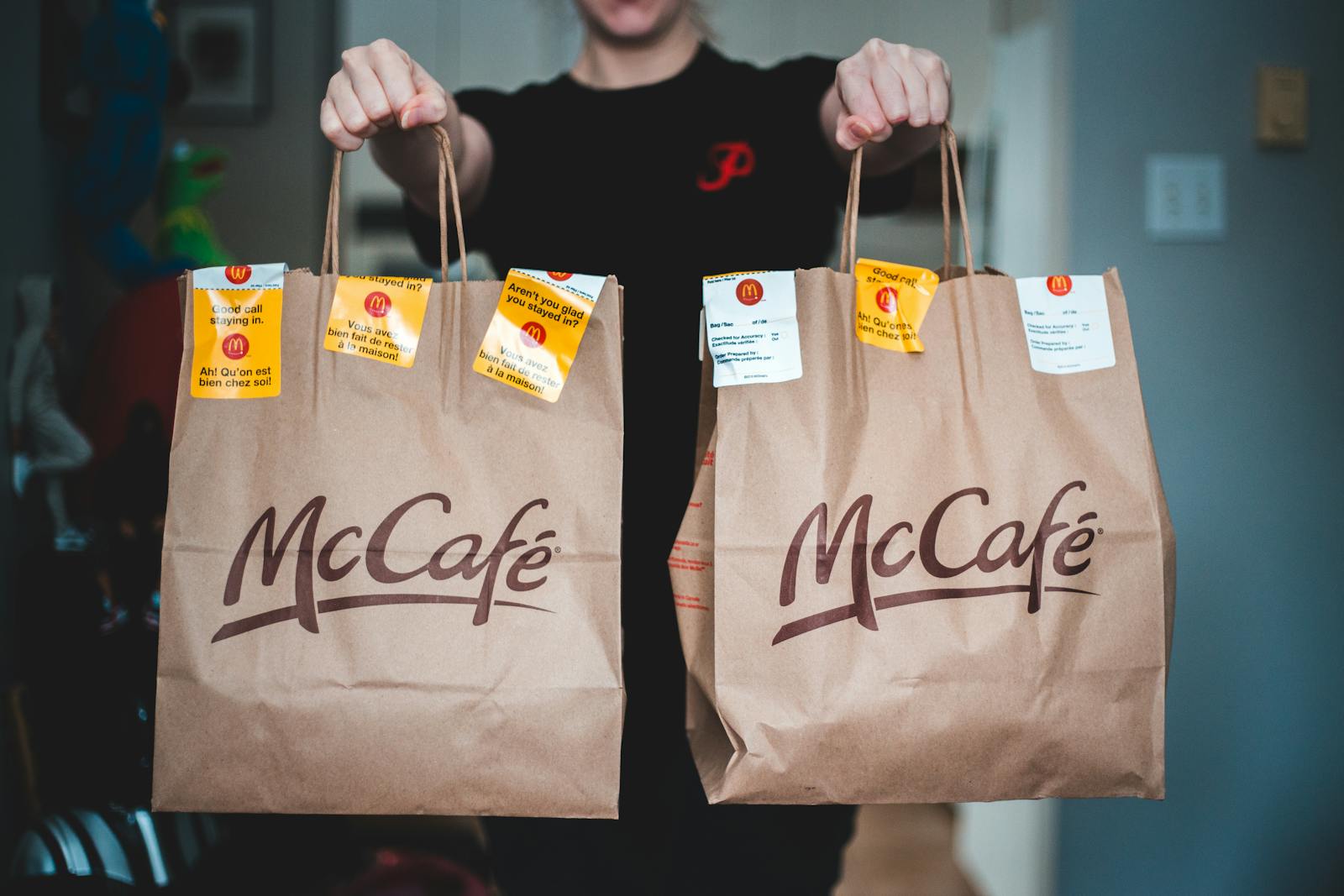 A person holds two McCafé food delivery bags indoors, emphasizing fast food service.