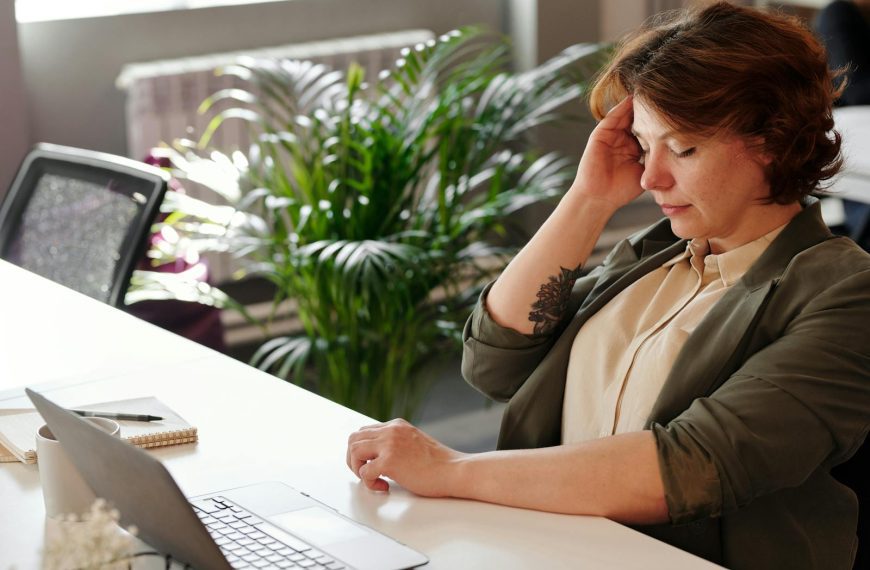 A businesswoman feeling stressed at her home office desk while working on her laptop.