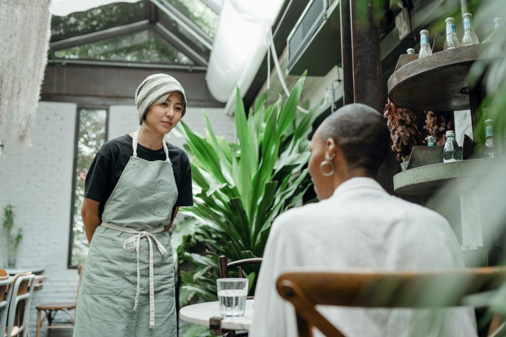 A waitress in a cozy cafe engaging in a friendly conversation with a seated customer.