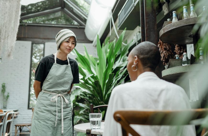 A waitress in a cozy cafe engaging in a friendly conversation with a seated customer.