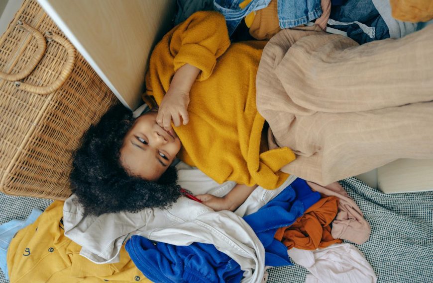 Adorable child lying contentedly in a pile of colorful cozy clothes indoors.