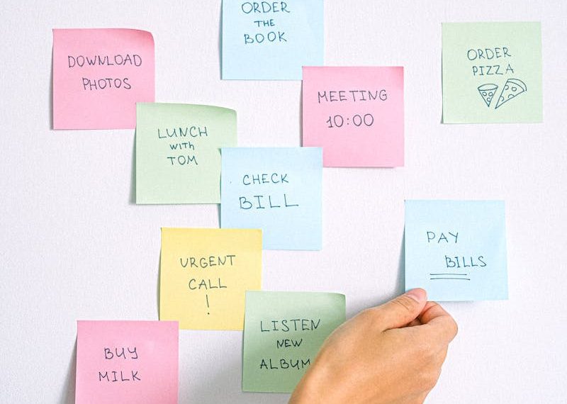A hand arranging colorful sticky notes with tasks on a white wall.