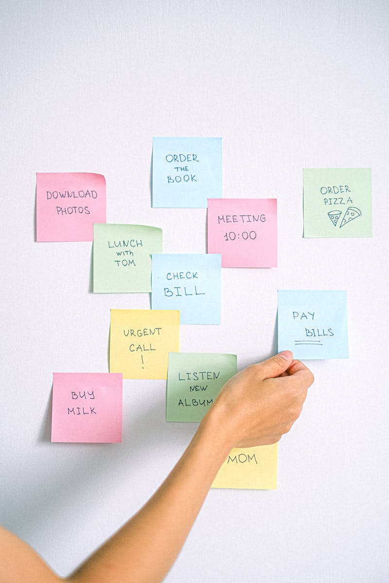 A hand arranging colorful sticky notes with tasks on a white wall.