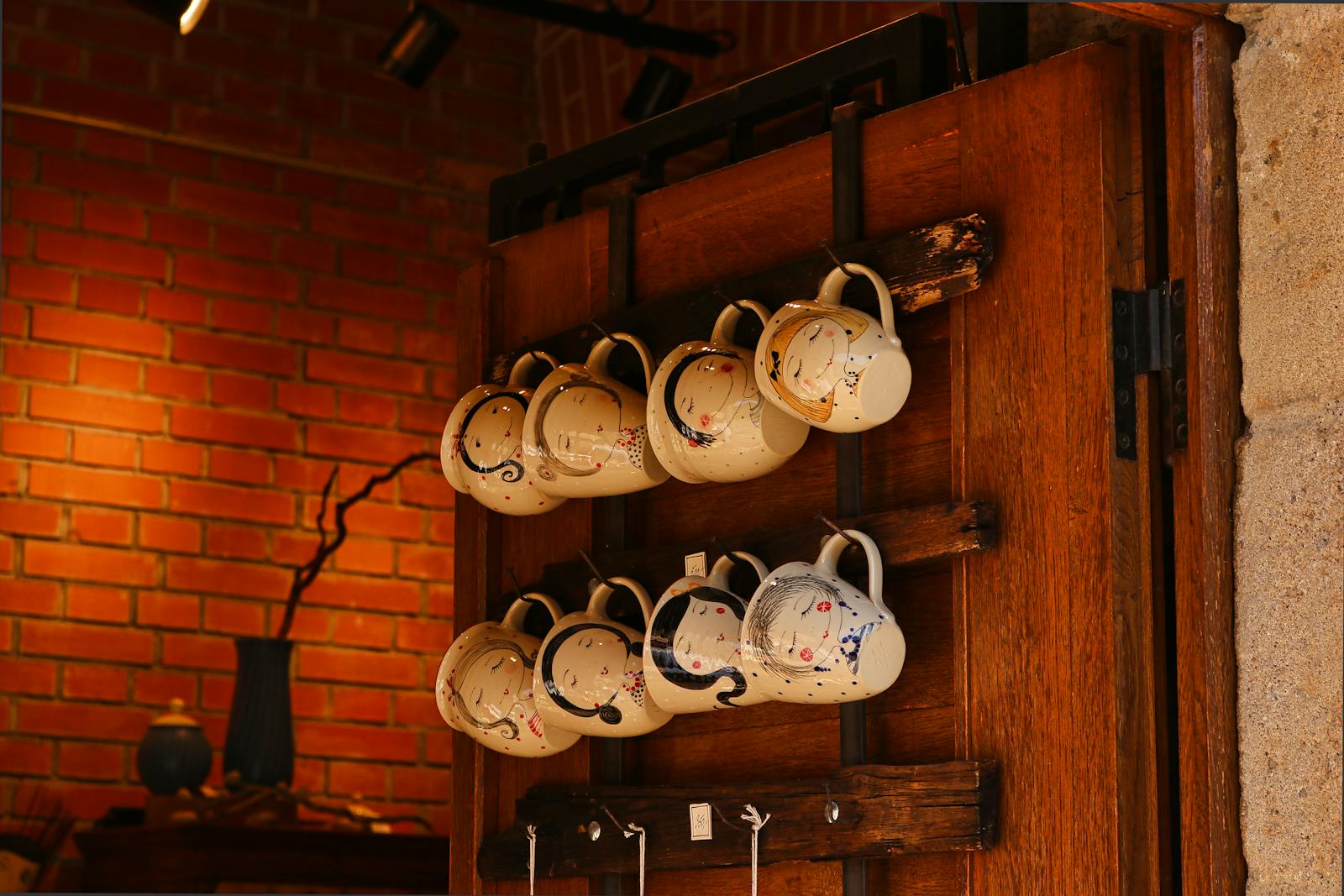Collection of vintage ceramic cups hanging on wooden shelf in cozy interior setting.