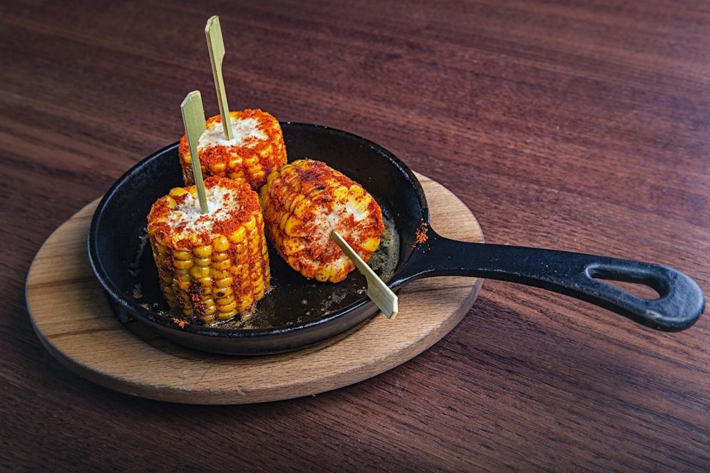 Delicious grilled corn skewers served on a cast iron skillet in a rustic cafe setting.