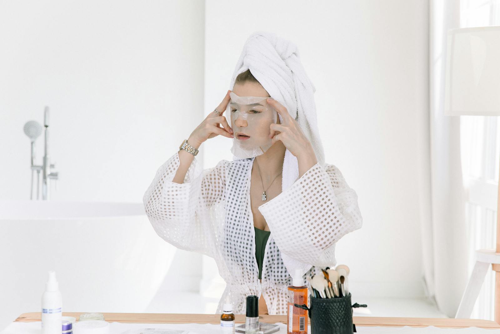 Woman applying a face mask in a bathroom, focusing on skincare and relaxation.