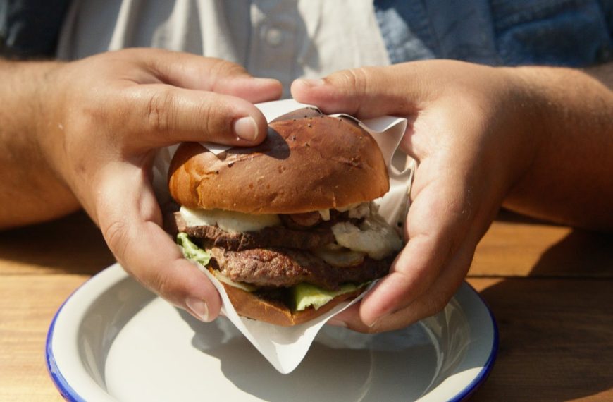 Hands holding a juicy grilled hamburger on a plate outdoors. Perfect for food enthusiasts.