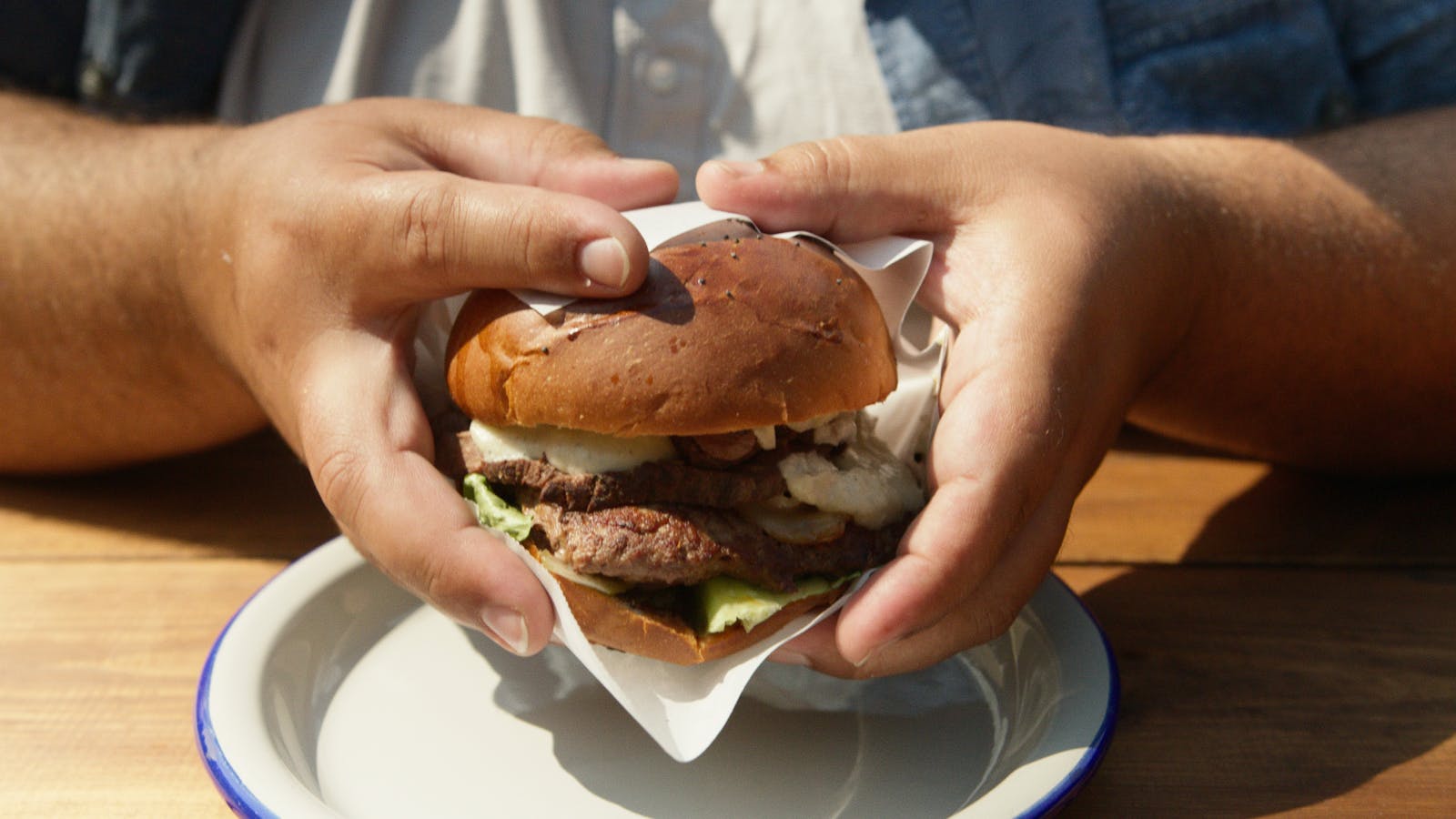 Hands holding a juicy grilled hamburger on a plate outdoors. Perfect for food enthusiasts.