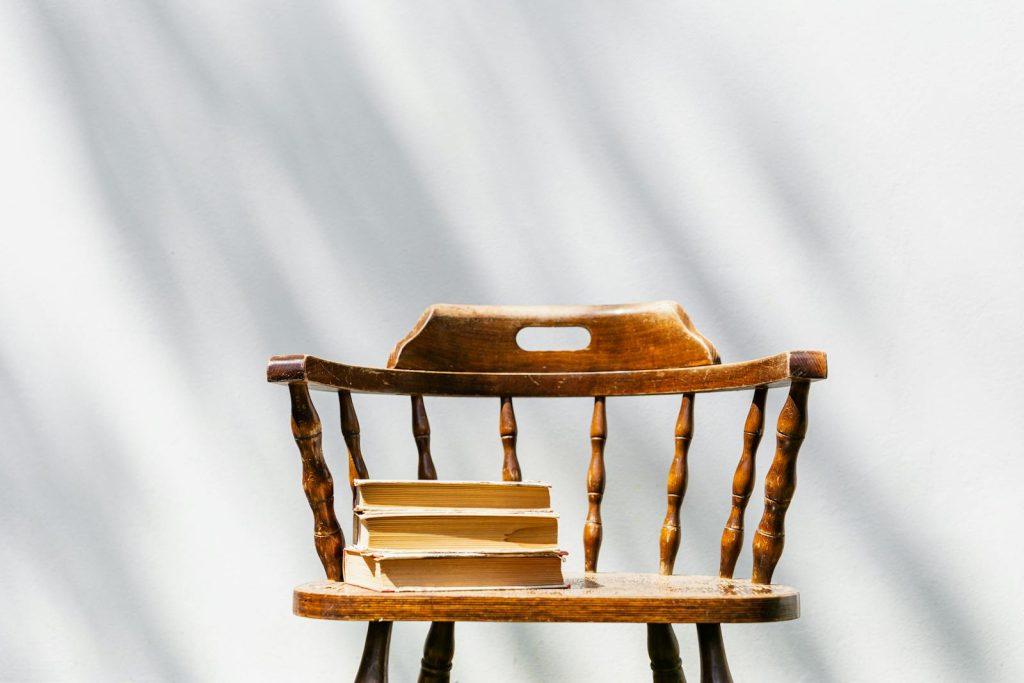 A vintage wooden chair holds a stack of books under sunlight indoors.