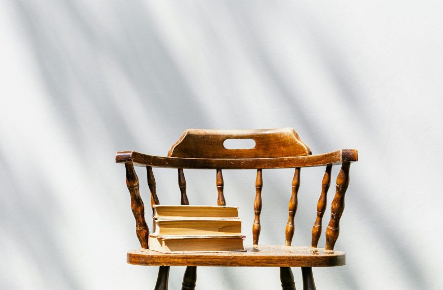 A vintage wooden chair holds a stack of books under sunlight indoors.