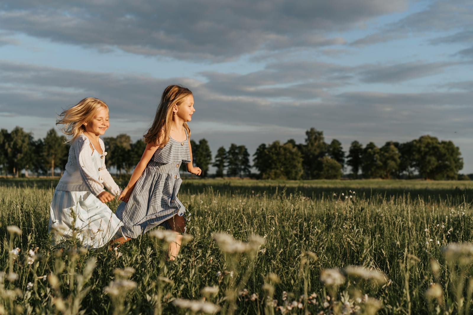 Two girls running happily in a sunny field, enjoying a carefree day outdoors.