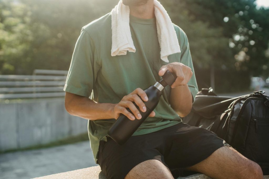 Close-up of a man sitting outdoors with a reusable water bottle and towel.