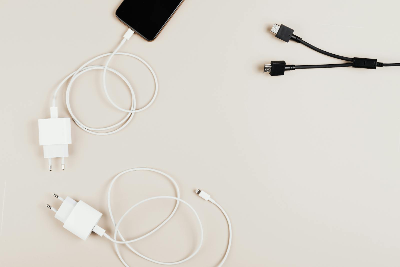 Flat lay of mobile devices with chargers and cables on a neutral background.