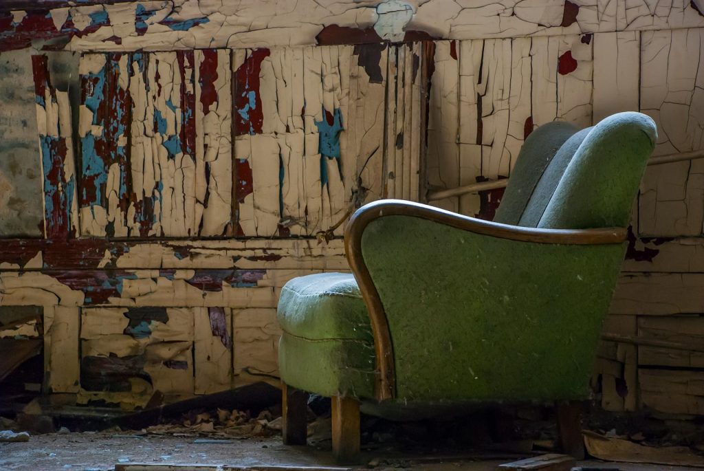 A rustic scene featuring an old armchair in an abandoned room with peeling paint walls.