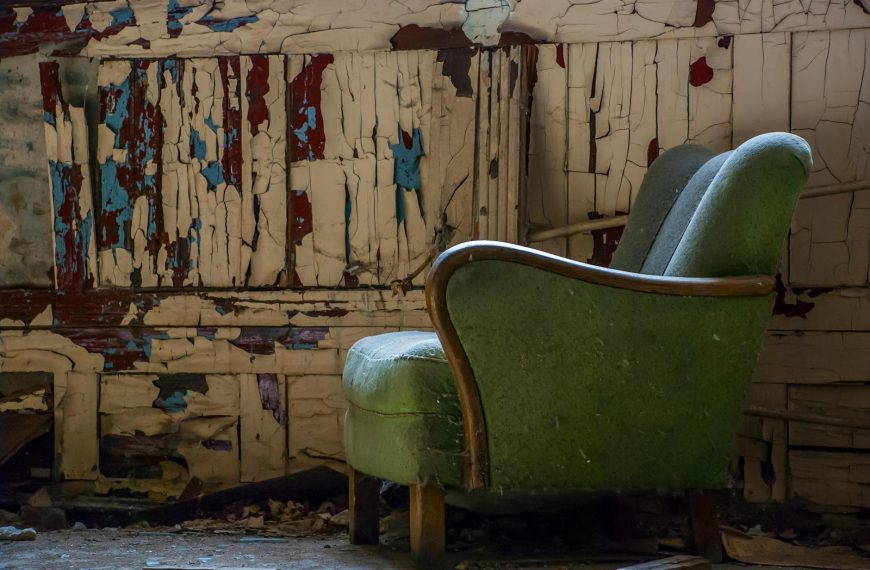 A rustic scene featuring an old armchair in an abandoned room with peeling paint walls.