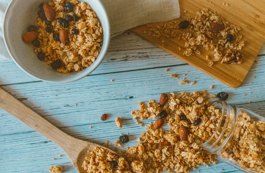 Top view of granola with almonds and berries spilled from a jar onto a wooden table.