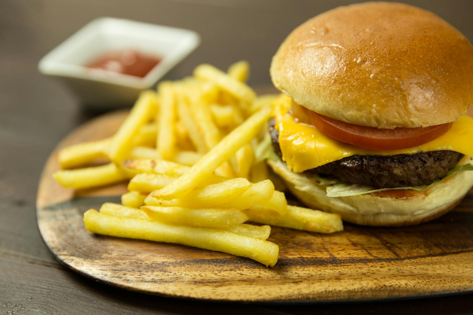 Delicious cheeseburger with fries and ketchup served on a wooden plate, perfect for lunch or snack.