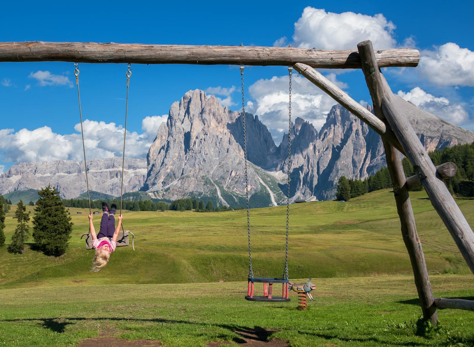 A child swings joyfully in an alpine meadow with the Dolomites in the background.