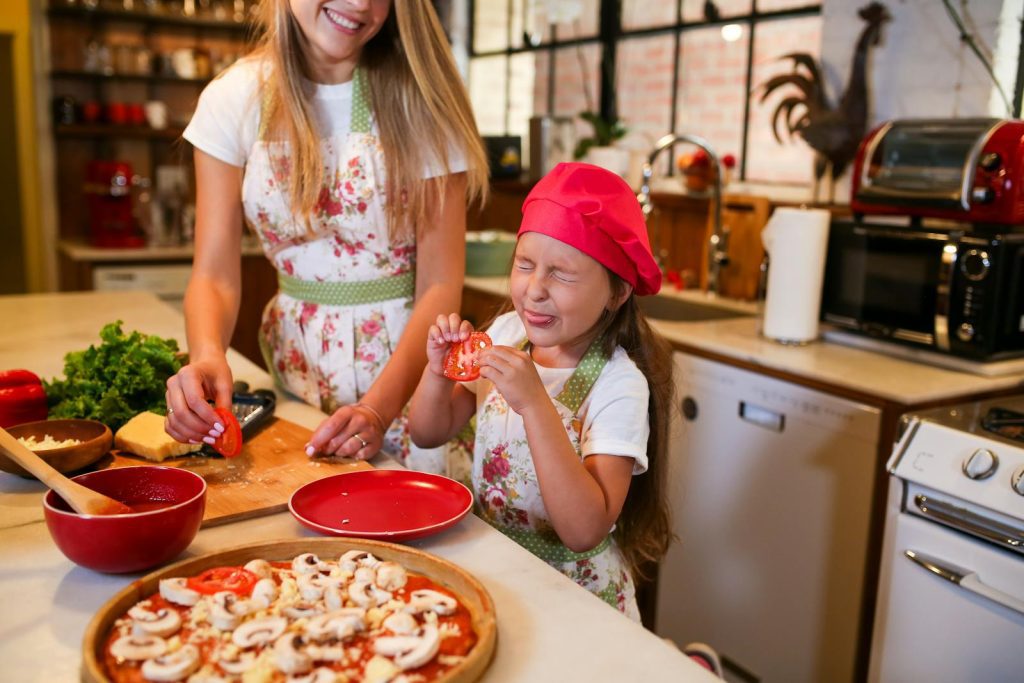 Happy mother and daughter making pizza together in a home kitchen, sharing quality family time.