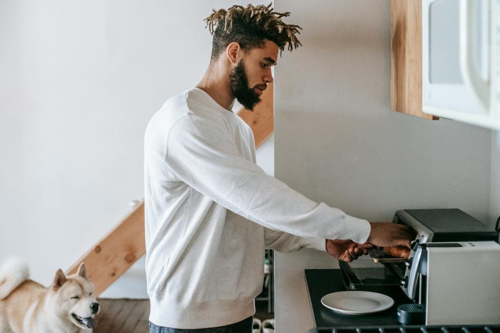 Young man using an oven toaster to prepare breakfast with his dog nearby in a cozy kitchen.
