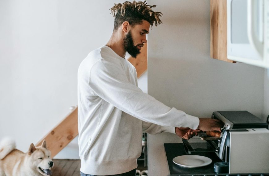 Young man using an oven toaster to prepare breakfast with his dog nearby in a cozy kitchen.