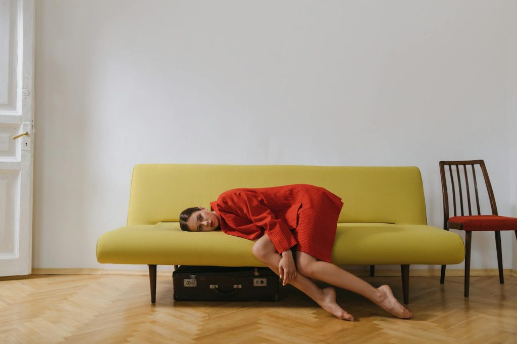 A woman in a red blazer rests on a minimalist yellow sofa indoors, evoking calmness.