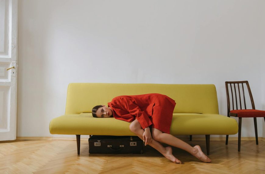 A woman in a red blazer rests on a minimalist yellow sofa indoors, evoking calmness.