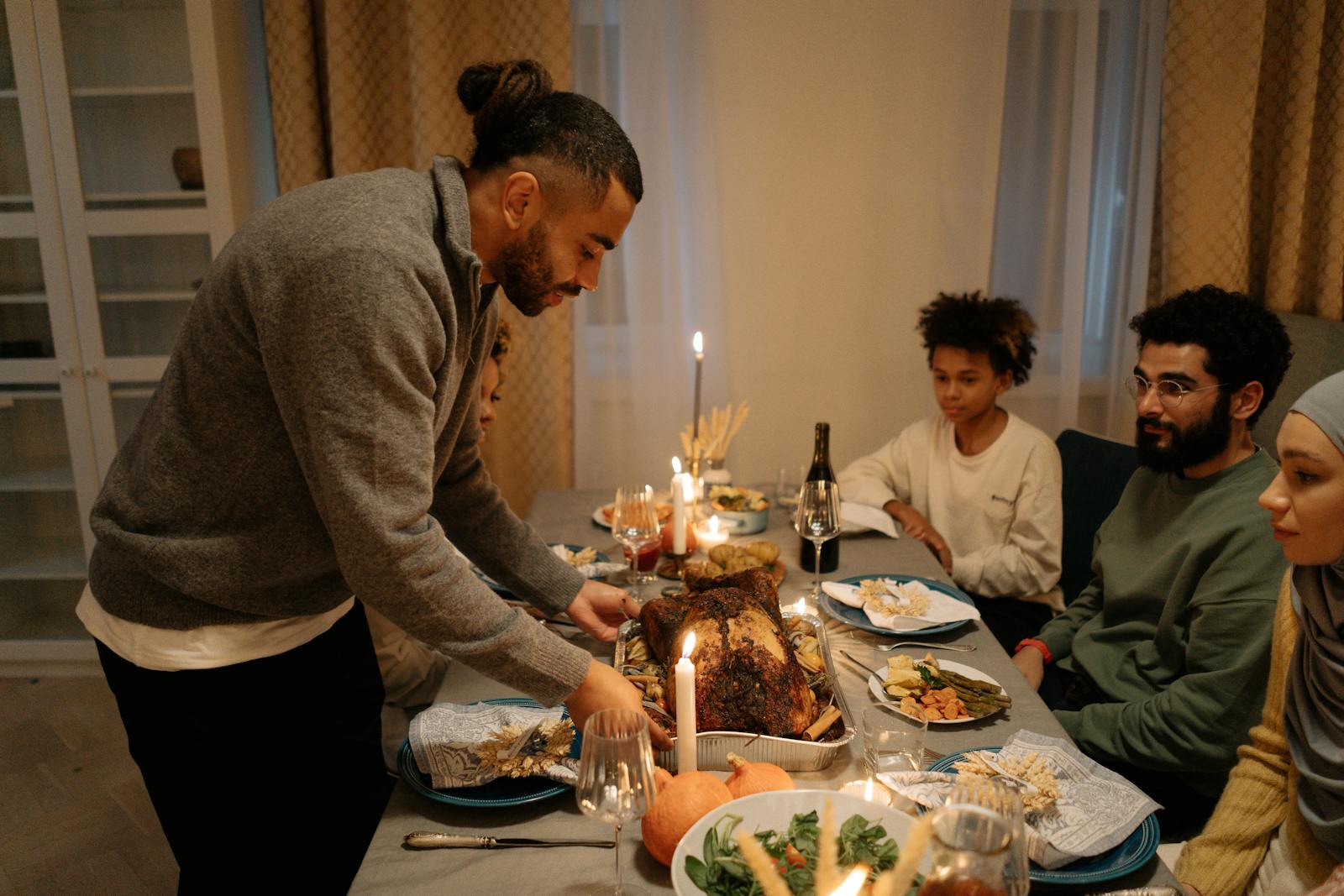 A family gathered around a dining table enjoying Thanksgiving dinner indoors with candlelit ambiance.