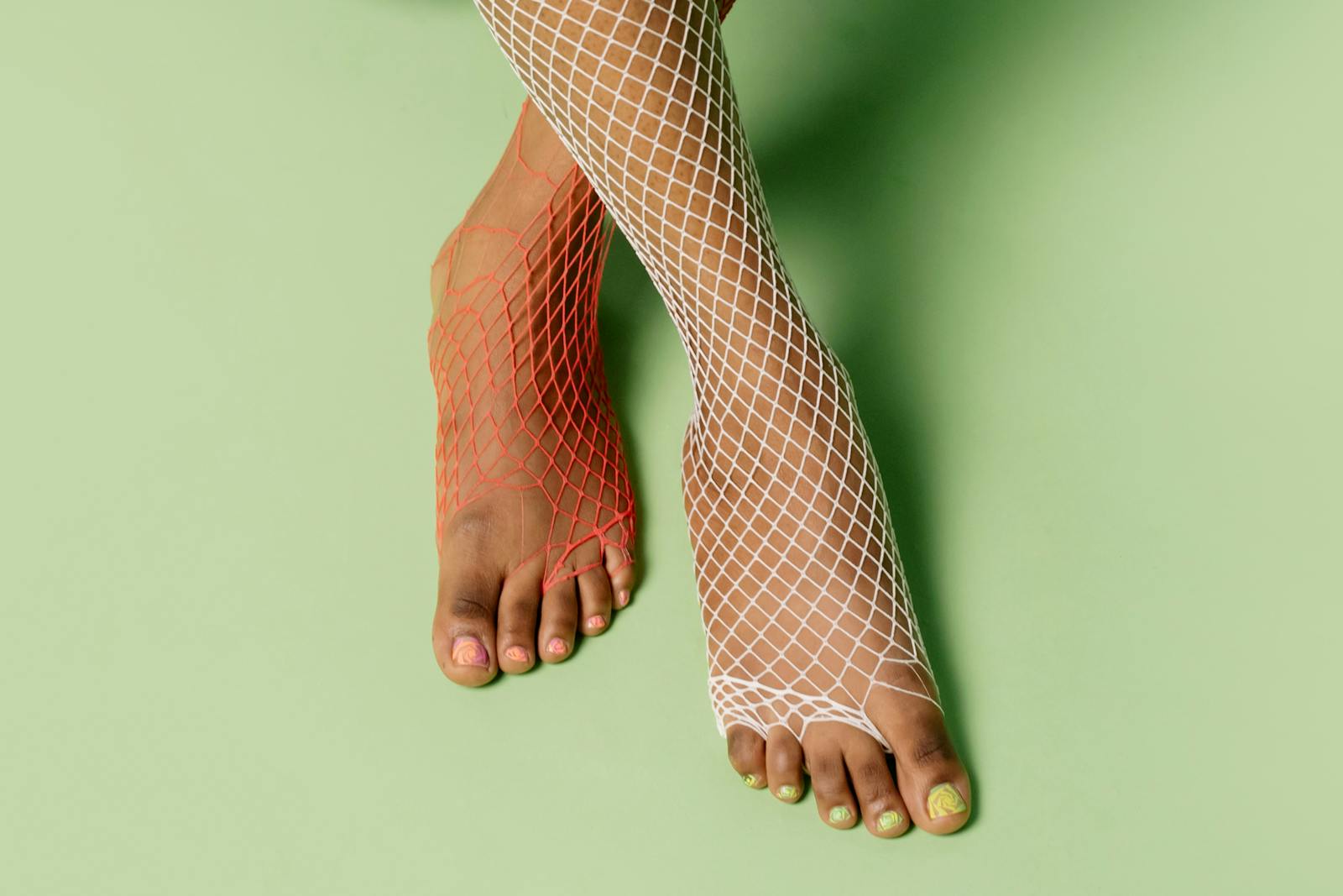 Close-up of vibrant feet in red and white fishnet stockings with manicured nails on green background.
