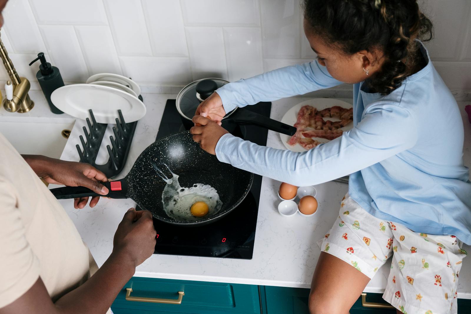 A child helps prepare breakfast, cracking eggs in a modern kitchen setting.