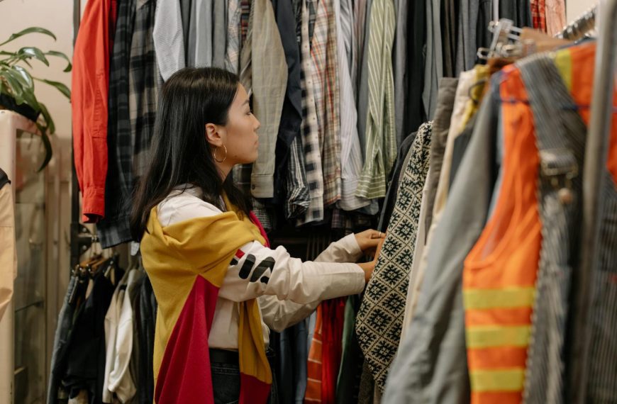 A young woman browsing clothes in a vintage store with colorful outfits.